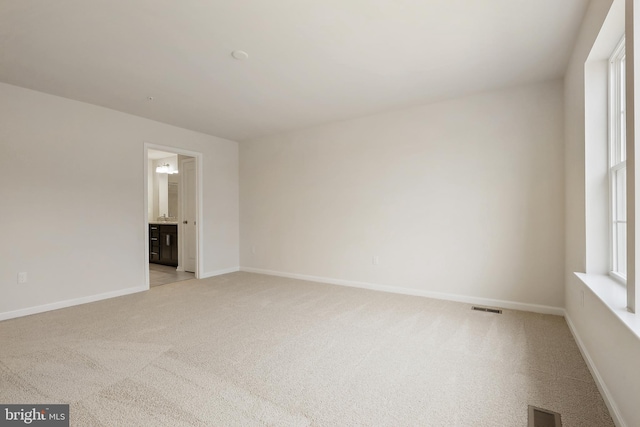 empty room featuring a wealth of natural light, visible vents, and light colored carpet