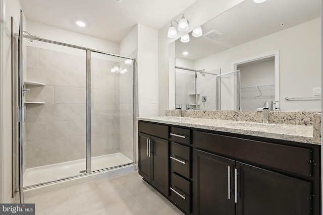 bathroom featuring a walk in closet, double vanity, a sink, a shower stall, and tile patterned flooring