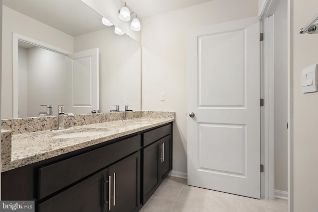 bathroom featuring double vanity, tile patterned flooring, a sink, and baseboards