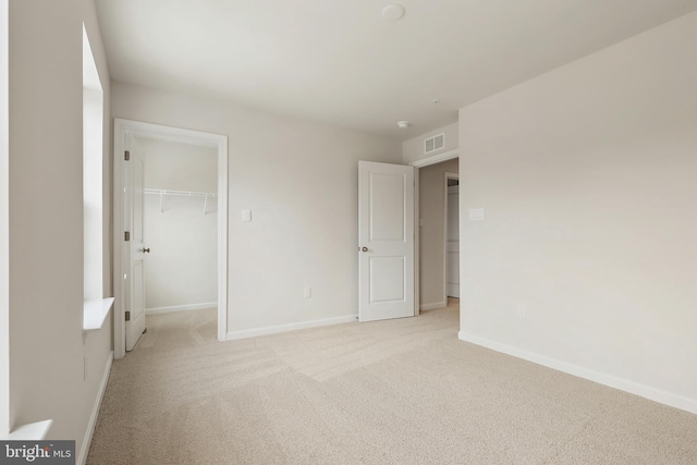 unfurnished bedroom featuring light colored carpet, visible vents, baseboards, a spacious closet, and a closet