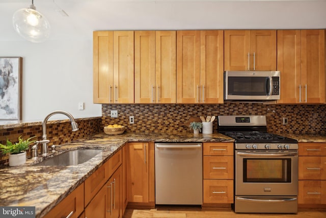 kitchen with appliances with stainless steel finishes, tasteful backsplash, sink, and dark stone counters