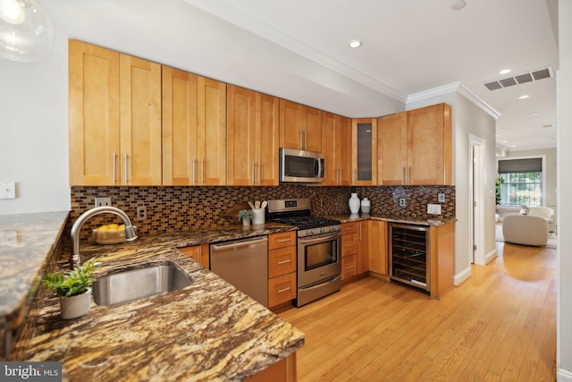 kitchen featuring light wood-type flooring, appliances with stainless steel finishes, beverage cooler, and dark stone counters