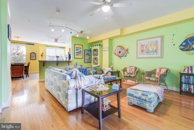 living area featuring light wood-style flooring, baseboards, and ceiling fan with notable chandelier