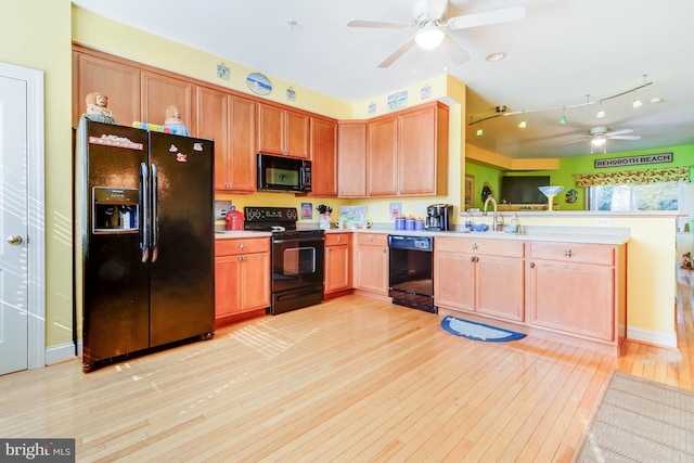 kitchen featuring a peninsula, light countertops, light wood-type flooring, black appliances, and a sink