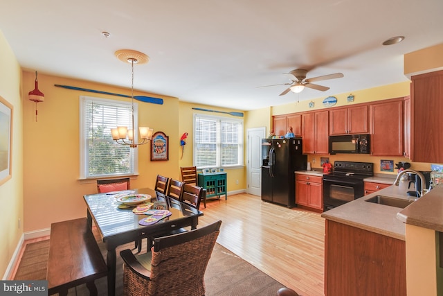 kitchen with a sink, brown cabinets, black appliances, light wood finished floors, and pendant lighting