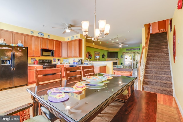 dining space with light wood-style floors, visible vents, stairway, and ceiling fan with notable chandelier