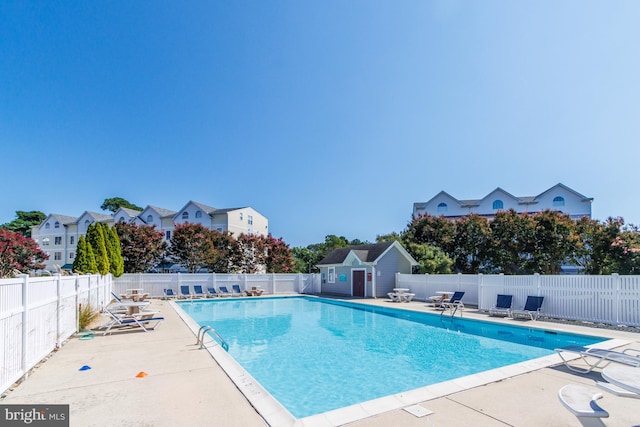 community pool with a patio area, a fenced backyard, and an outdoor structure