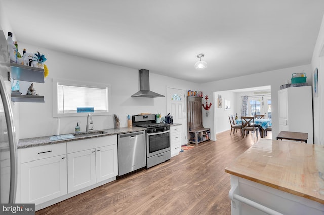 kitchen featuring open shelves, a sink, white cabinets, appliances with stainless steel finishes, and wall chimney exhaust hood