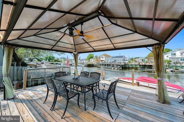 deck featuring a gazebo, outdoor dining area, a ceiling fan, and a water view