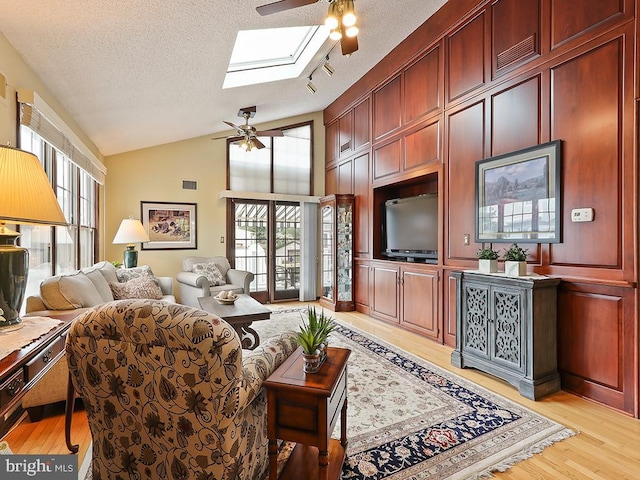 living room with a textured ceiling, light hardwood / wood-style flooring, ceiling fan, and a skylight