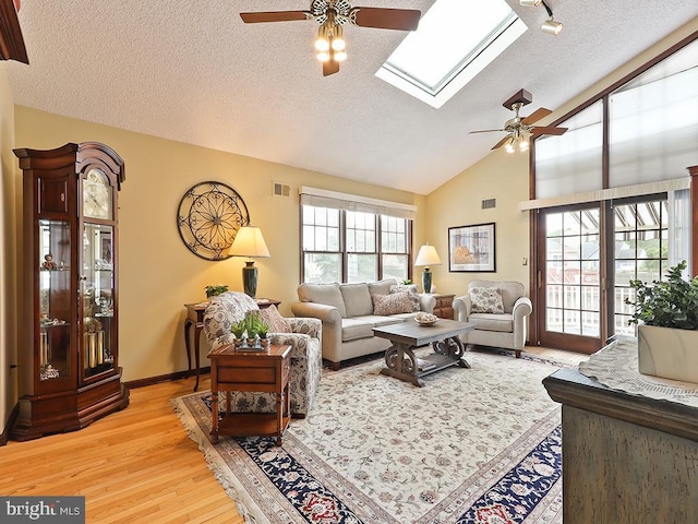 living room with high vaulted ceiling, a textured ceiling, a skylight, light hardwood / wood-style flooring, and ceiling fan