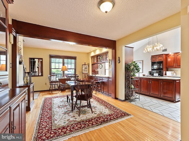 dining area with a textured ceiling, light hardwood / wood-style flooring, a notable chandelier, and vaulted ceiling with beams