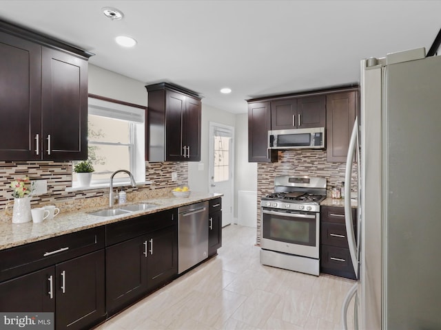 kitchen with backsplash, light stone countertops, dark brown cabinetry, appliances with stainless steel finishes, and a sink