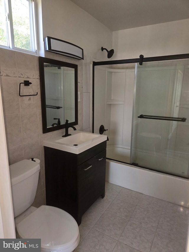 full bathroom featuring tile patterned flooring, toilet, shower / bath combination with glass door, tile walls, and vanity