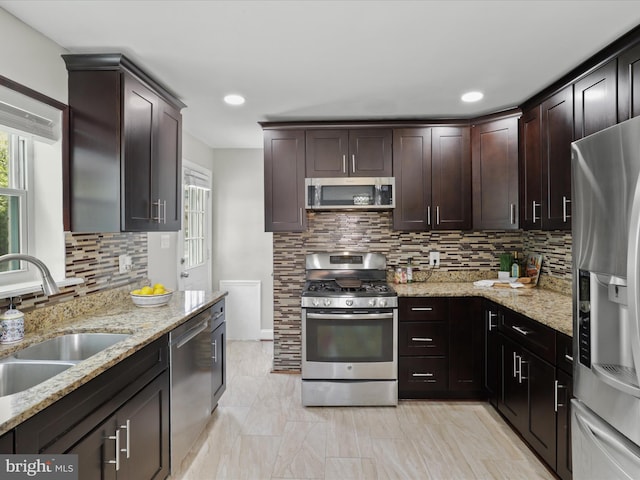 kitchen featuring light stone countertops, a sink, dark brown cabinets, appliances with stainless steel finishes, and tasteful backsplash