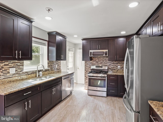 kitchen featuring tasteful backsplash, dark brown cabinets, light stone countertops, stainless steel appliances, and a sink