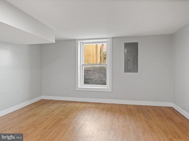 unfurnished room with electric panel, light wood-style floors, and baseboards