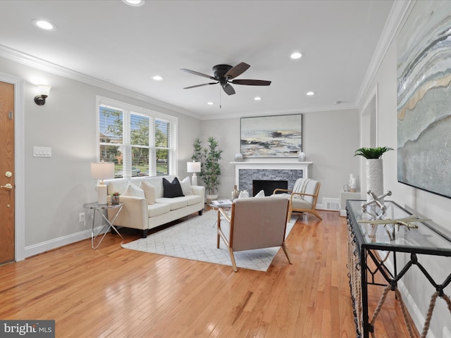 living area featuring recessed lighting, light wood-style flooring, a stone fireplace, and ornamental molding