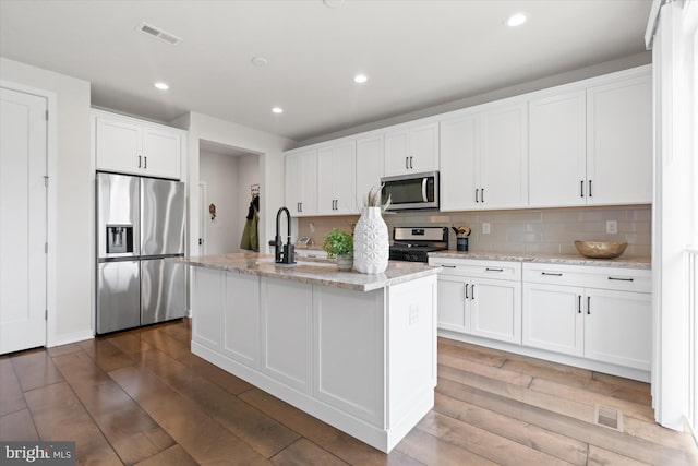 kitchen with decorative backsplash, hardwood / wood-style floors, an island with sink, white cabinetry, and stainless steel appliances