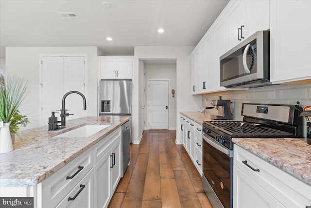 kitchen with decorative backsplash, wood-type flooring, appliances with stainless steel finishes, light stone counters, and sink