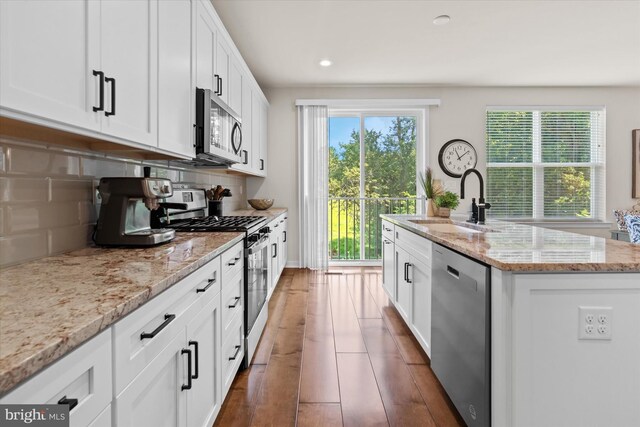 kitchen with backsplash, a center island with sink, appliances with stainless steel finishes, and plenty of natural light