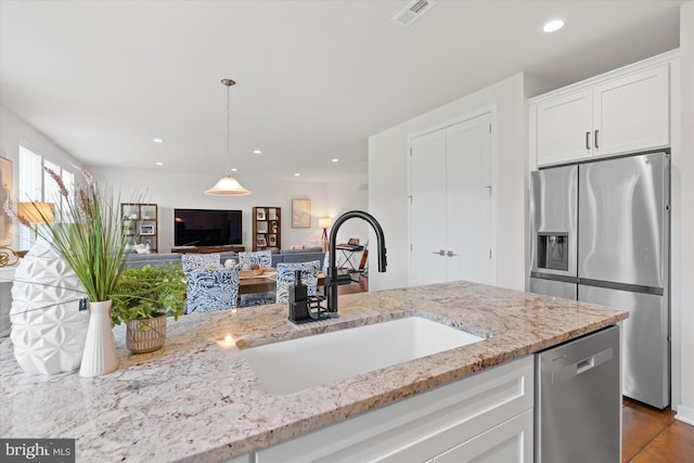 kitchen with sink, appliances with stainless steel finishes, light stone counters, white cabinetry, and hanging light fixtures