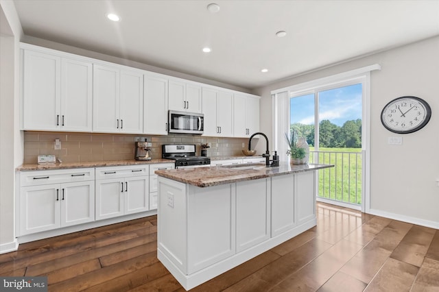 kitchen featuring white cabinets, decorative backsplash, a kitchen island with sink, and gas range oven