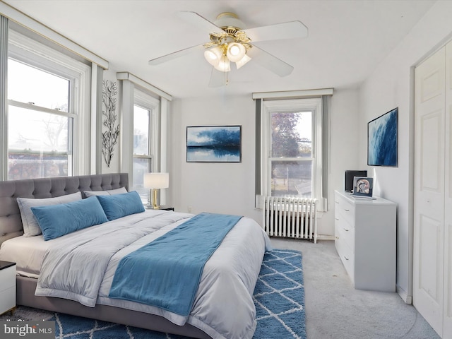 bedroom featuring radiator, ceiling fan, light carpet, and multiple windows