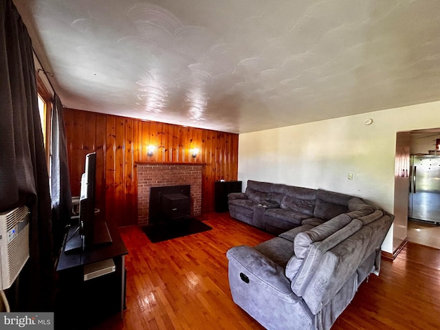 living room with a brick fireplace, wood walls, and wood finished floors