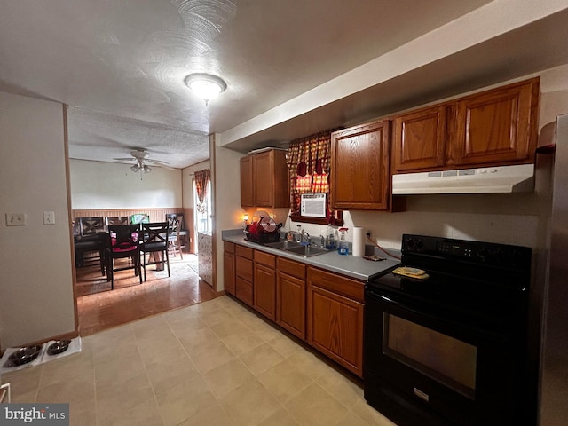 kitchen featuring brown cabinetry, black electric range oven, light countertops, under cabinet range hood, and a sink