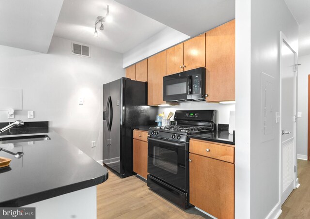 kitchen with light wood-type flooring, black appliances, kitchen peninsula, and a breakfast bar