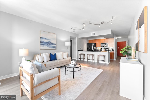 living room with light wood-style floors, track lighting, visible vents, and baseboards