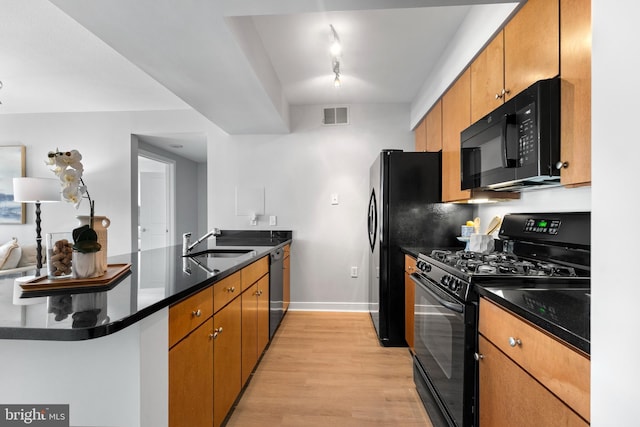 kitchen with light wood-type flooring, black appliances, kitchen peninsula, and sink