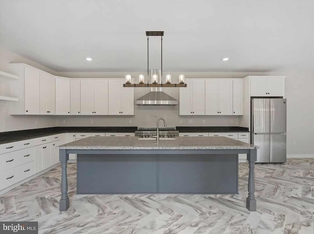 kitchen featuring an island with sink, stainless steel refrigerator, a kitchen breakfast bar, and wall chimney range hood