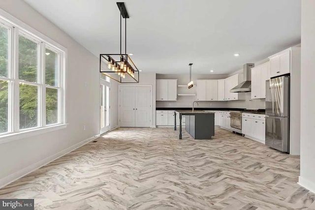 kitchen featuring an island with sink, a kitchen bar, stainless steel appliances, white cabinetry, and wall chimney range hood