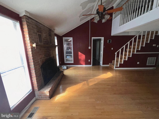 unfurnished living room with brick wall, a textured ceiling, wood-type flooring, ceiling fan, and a brick fireplace