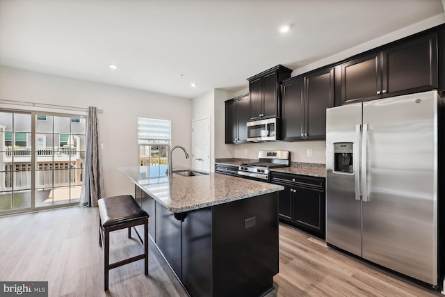 kitchen with light hardwood / wood-style flooring, light stone counters, a kitchen island with sink, a breakfast bar area, and stainless steel appliances