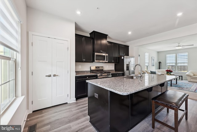 kitchen featuring stainless steel appliances, light hardwood / wood-style floors, sink, an island with sink, and ceiling fan