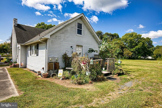 view of side of home featuring a shingled roof, a chimney, and a yard