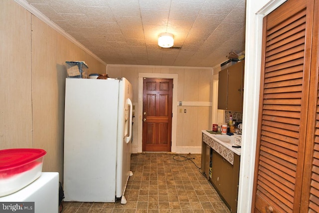 kitchen with wooden walls, ornamental molding, sink, and white refrigerator