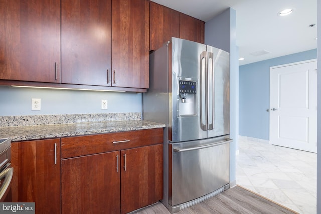 kitchen featuring light wood-type flooring, light stone counters, and stainless steel refrigerator with ice dispenser