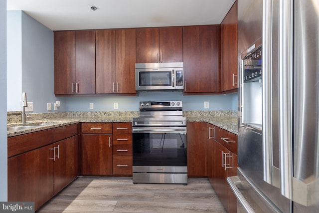 kitchen with sink, light hardwood / wood-style floors, light stone counters, and stainless steel appliances