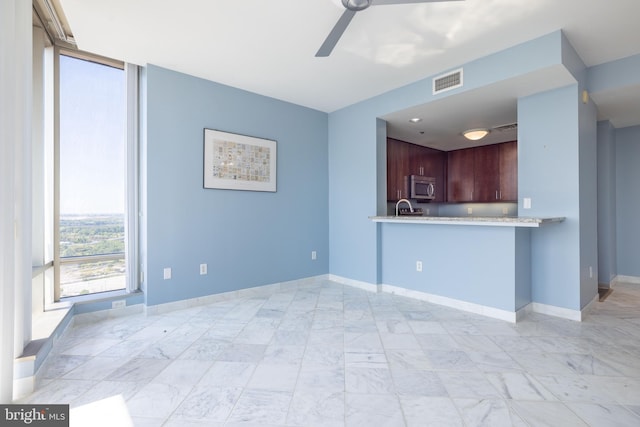 unfurnished living room with a ceiling fan, a wall of windows, visible vents, and baseboards