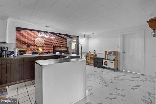 kitchen featuring sink, brick wall, light tile patterned flooring, and white cabinetry