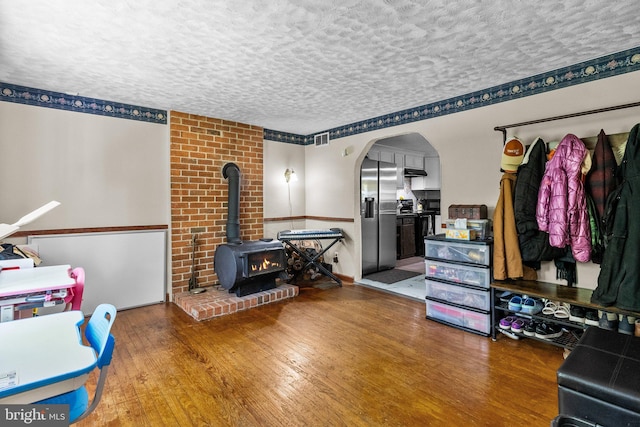 interior space with a textured ceiling, brick wall, a wood stove, and wood-type flooring