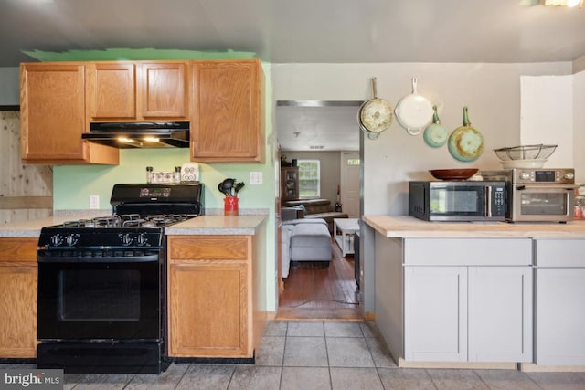 kitchen with black range with gas cooktop, stainless steel microwave, light countertops, under cabinet range hood, and light tile patterned flooring