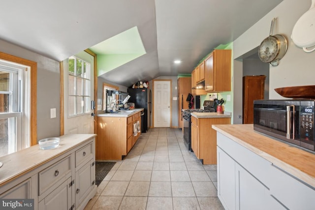 kitchen with vaulted ceiling, light countertops, black appliances, white cabinetry, and light tile patterned flooring