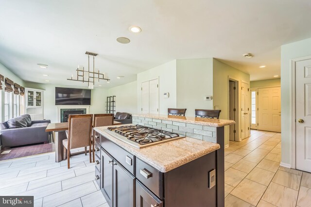 kitchen featuring stainless steel gas cooktop, dark brown cabinets, a center island, light stone countertops, and hanging light fixtures