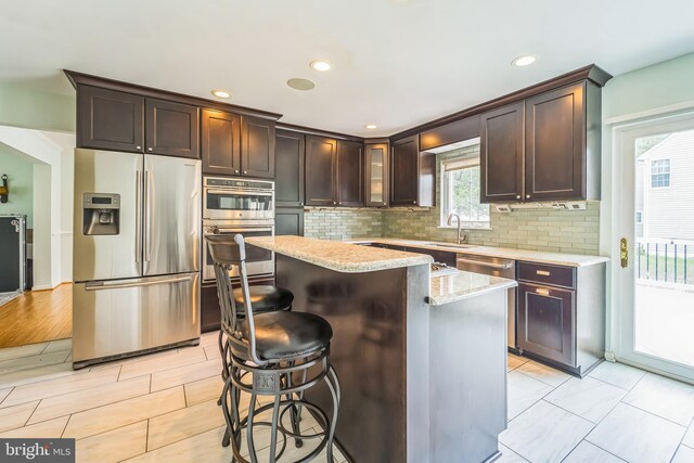 kitchen with light stone countertops, appliances with stainless steel finishes, light hardwood / wood-style floors, a center island, and decorative backsplash