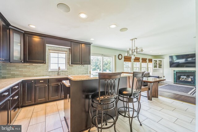 kitchen with a kitchen island, light stone countertops, backsplash, and dark brown cabinets